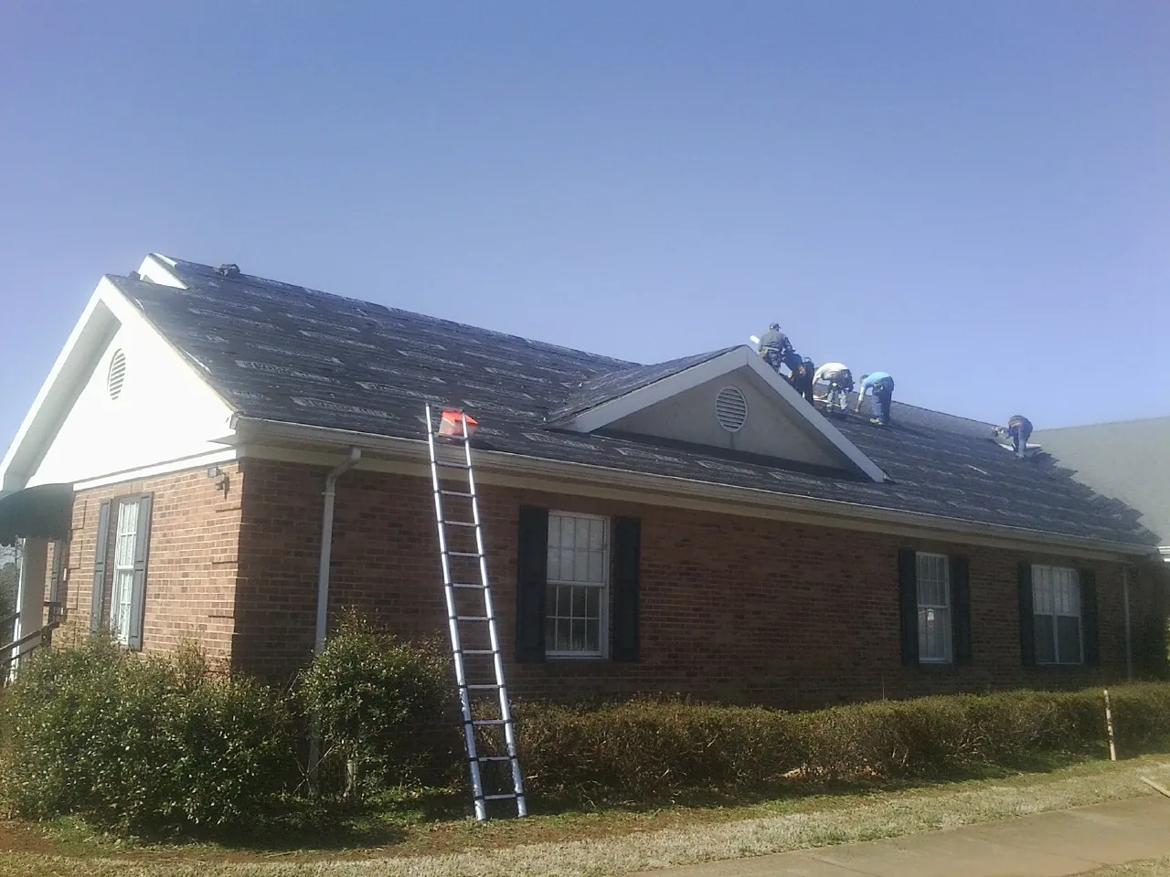 Crew tearing shingles off a brick ranch roof with a ladder set — Metal Roof Repair work by our crew in Gravel Switch