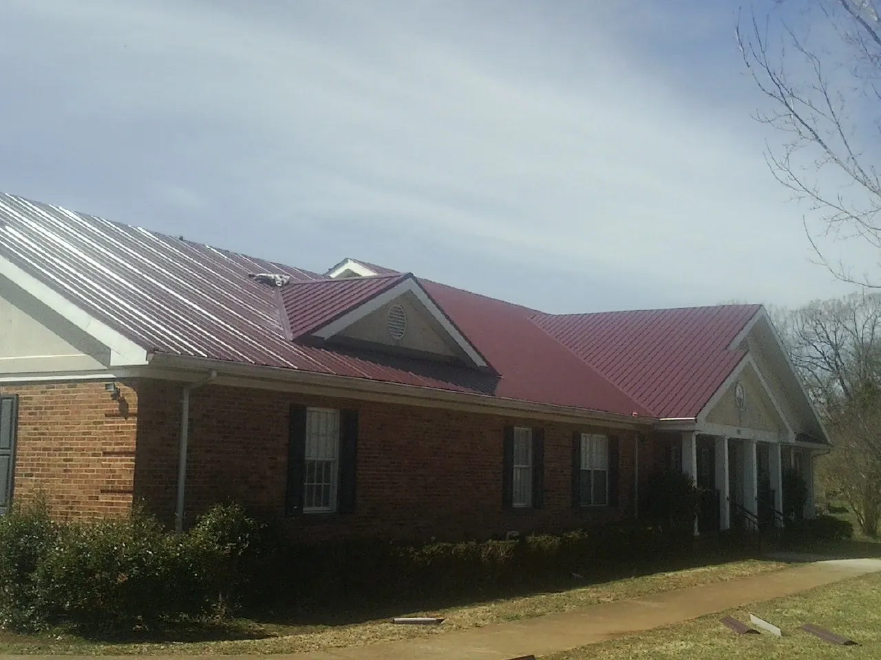 Red metal roof with gabled entries on a long brick building, from a Hail Damage Roof Repair job in Gravel Switch