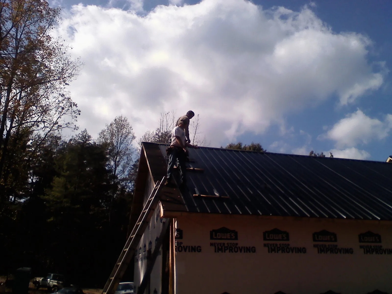 Roofer fastening dark metal panels high against a cloudy sky, from a Roof Inspection job in Gravel Switch