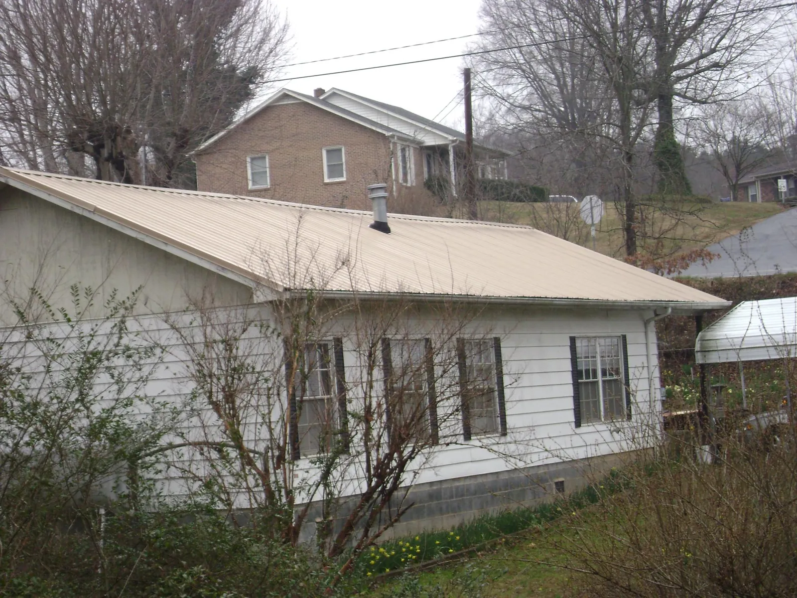Tan metal roof on a white sided house set into a hillside — Commercial Roofing by Roofing Brothers in Gravel Switch
